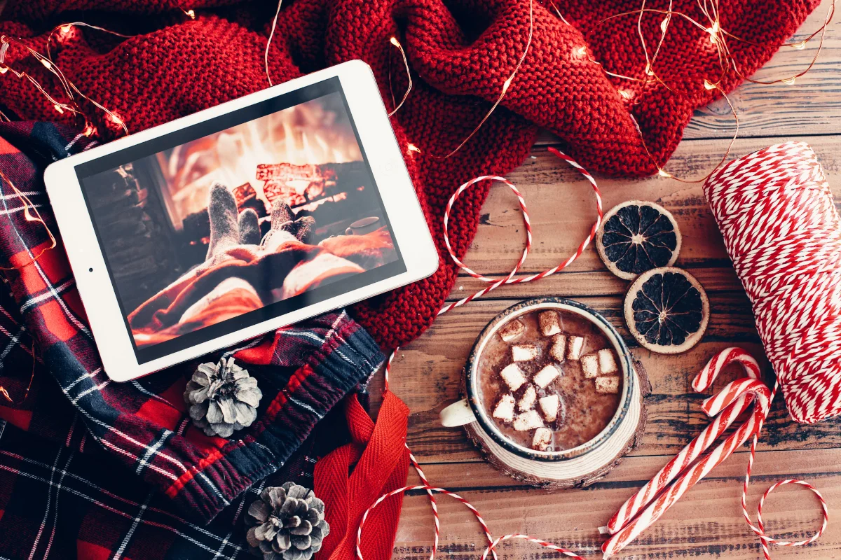 Tablet and hot cocoa surrounded by red blankets and candy canes