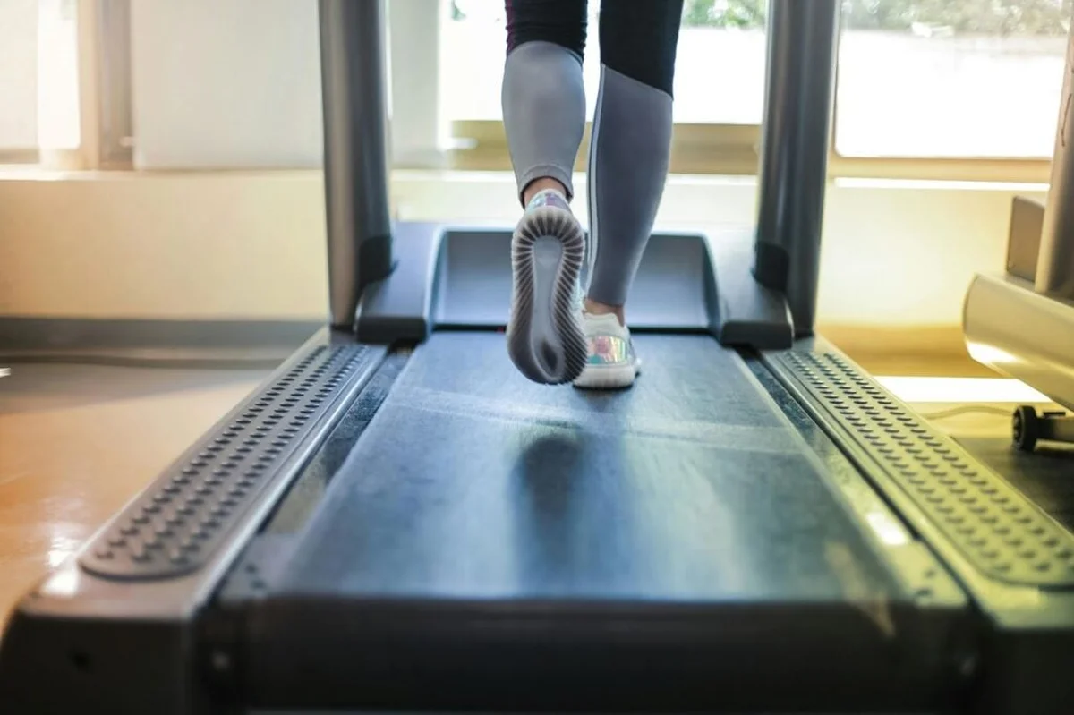 Legs walking on a treadmill in a bright indoor gym