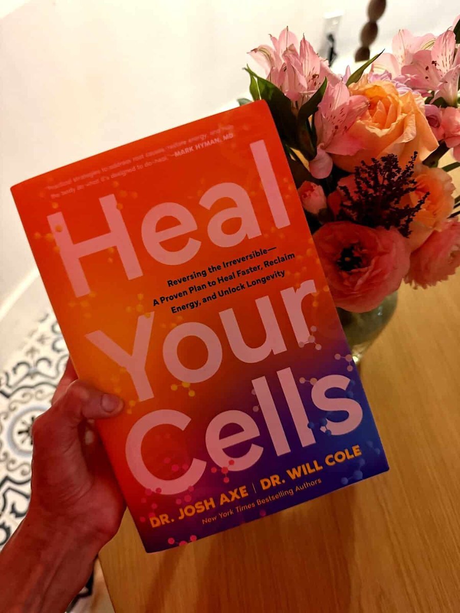 Hand holding the Heal Your Cells book near flowers