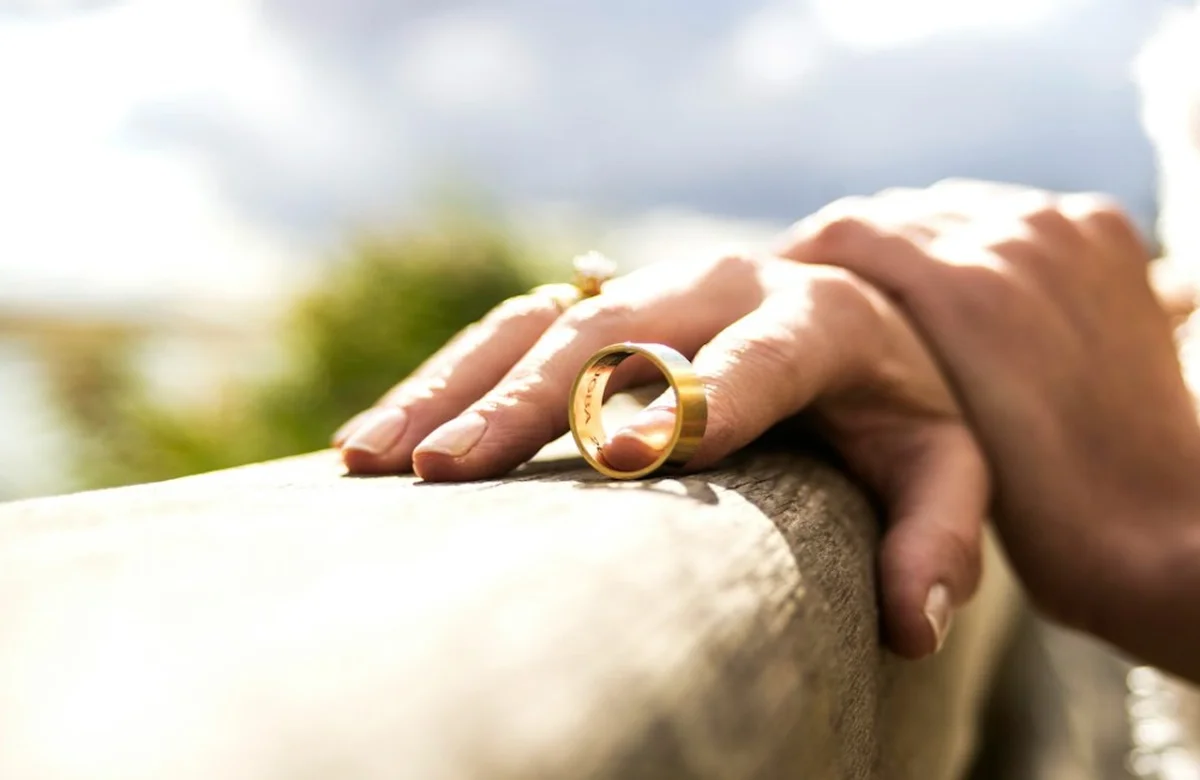 Couple's hands resting together with a gold wedding ring between them